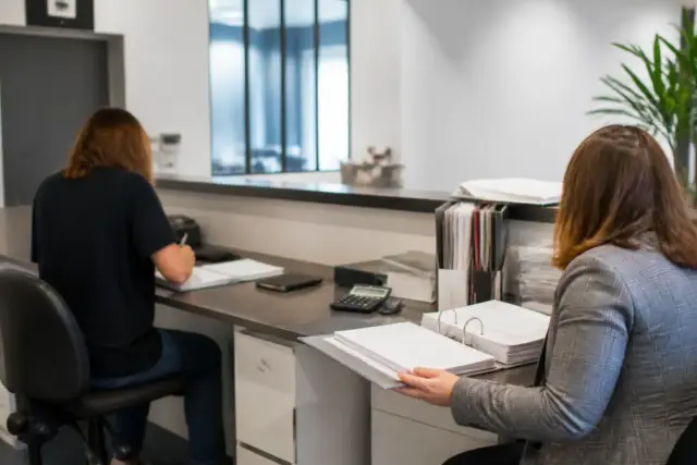 Deux personnes à un comptoir d’atelier, l’une au poste de travail, l’autre à la comptabilité, un dossier de déclaration ouvert devant elles