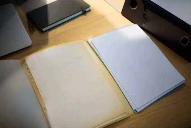 Ancien courrier à en-tête de régime social posé sur un bureau à côté d’un dossier récent, la date soulignée au crayon