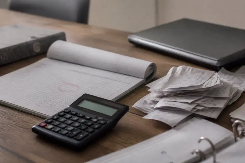 Carnet de factures et calculatrice sur un comptoir, le total hors taxe d’un mois entouré, une pile de reçus à côté