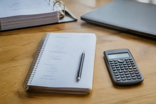 Cascade de soldes calculés à la main sur un cahier, chaque ligne reliée à la suivante par une flèche, calculatrice à côté