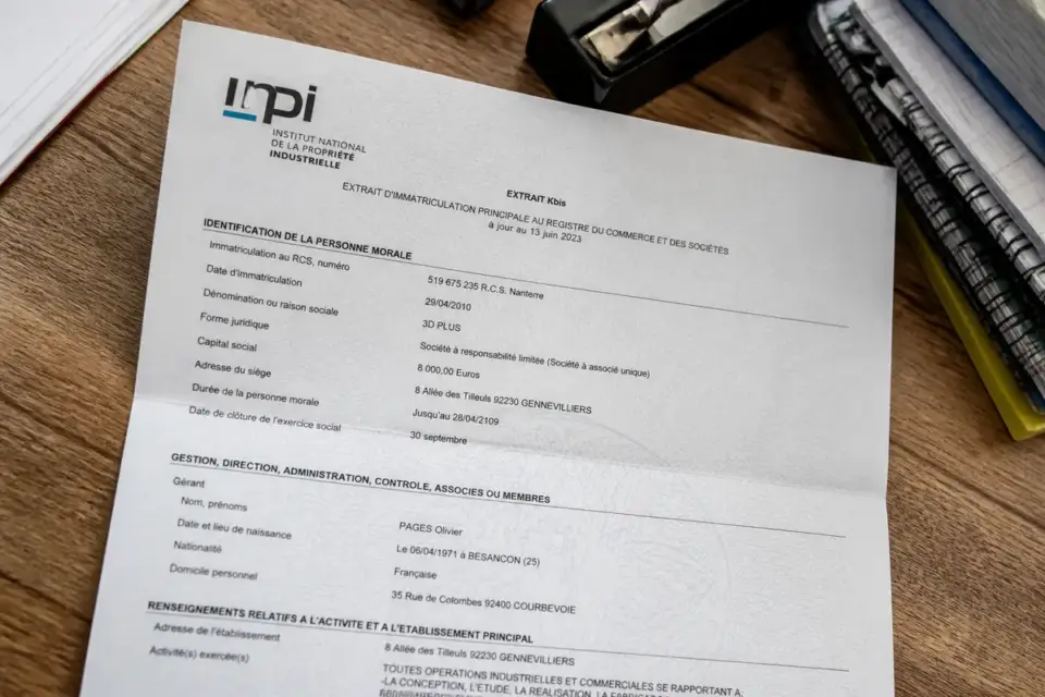 Document Kbis sur une table en bois avec des dossiers et un agrafeuse adjacents