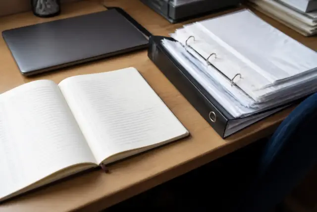 Cahier de recettes ouvert avec des lignes manuscrites de dates et de montants, à côté d’un classeur de factures