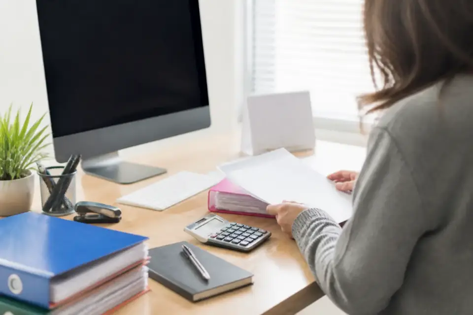 Poste de travail avec une déclaration de TVA affichée à l’écran, un calendrier papier et une calculatrice à côté